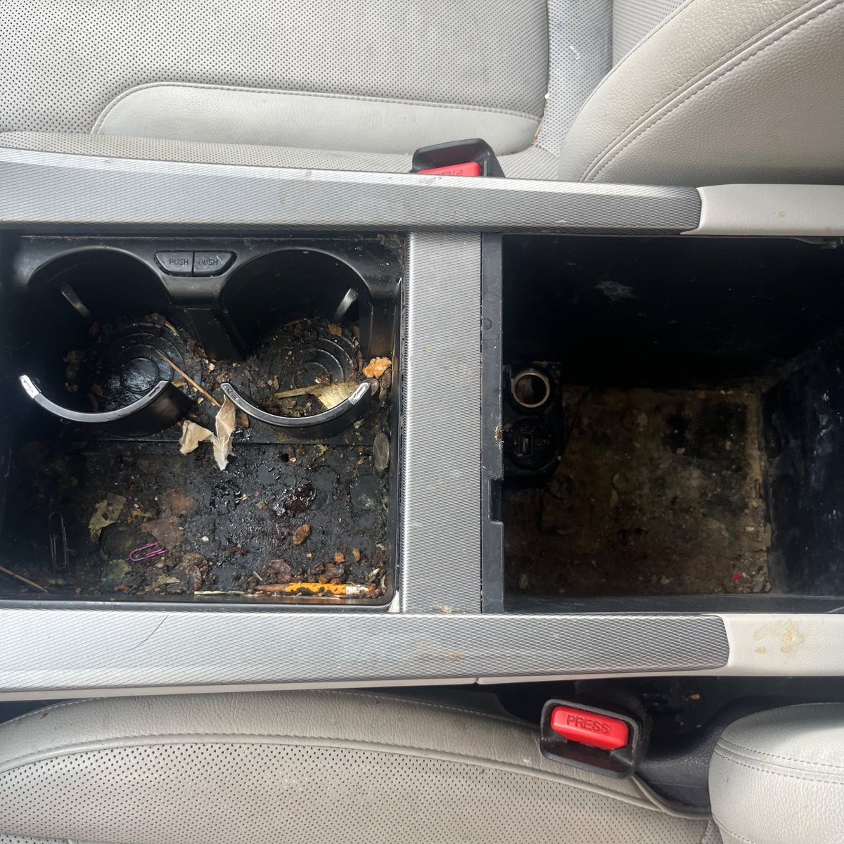 A rear centre console with the cupholders full of spilled food and debris before cleaning